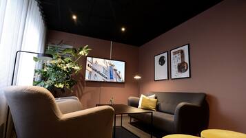 Un salon moderne avec un canapé, un fauteuil et un pouf, un téléviseur à écran plat, une plante en pot et des œuvres d’art encadrées accrochées au mur.
