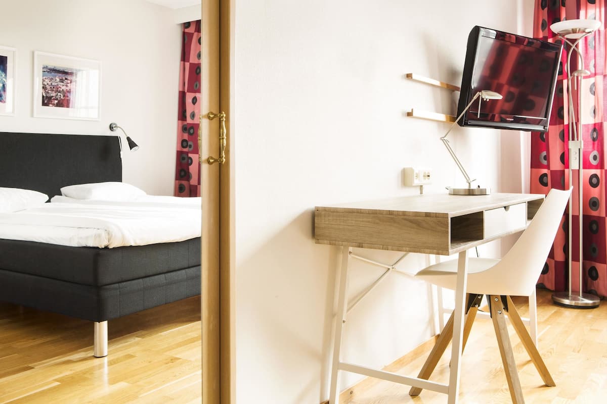A bedroom with a bed, a desk, a chair, a TV, and a curtain.