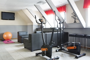 Un gimnasio con equipo de ejercicio, una pelota grande y un televisor en la pared.