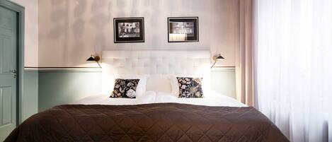 A neatly made bed with a brown quilt, two pillows with floral designs, and two framed pictures on the wall above.