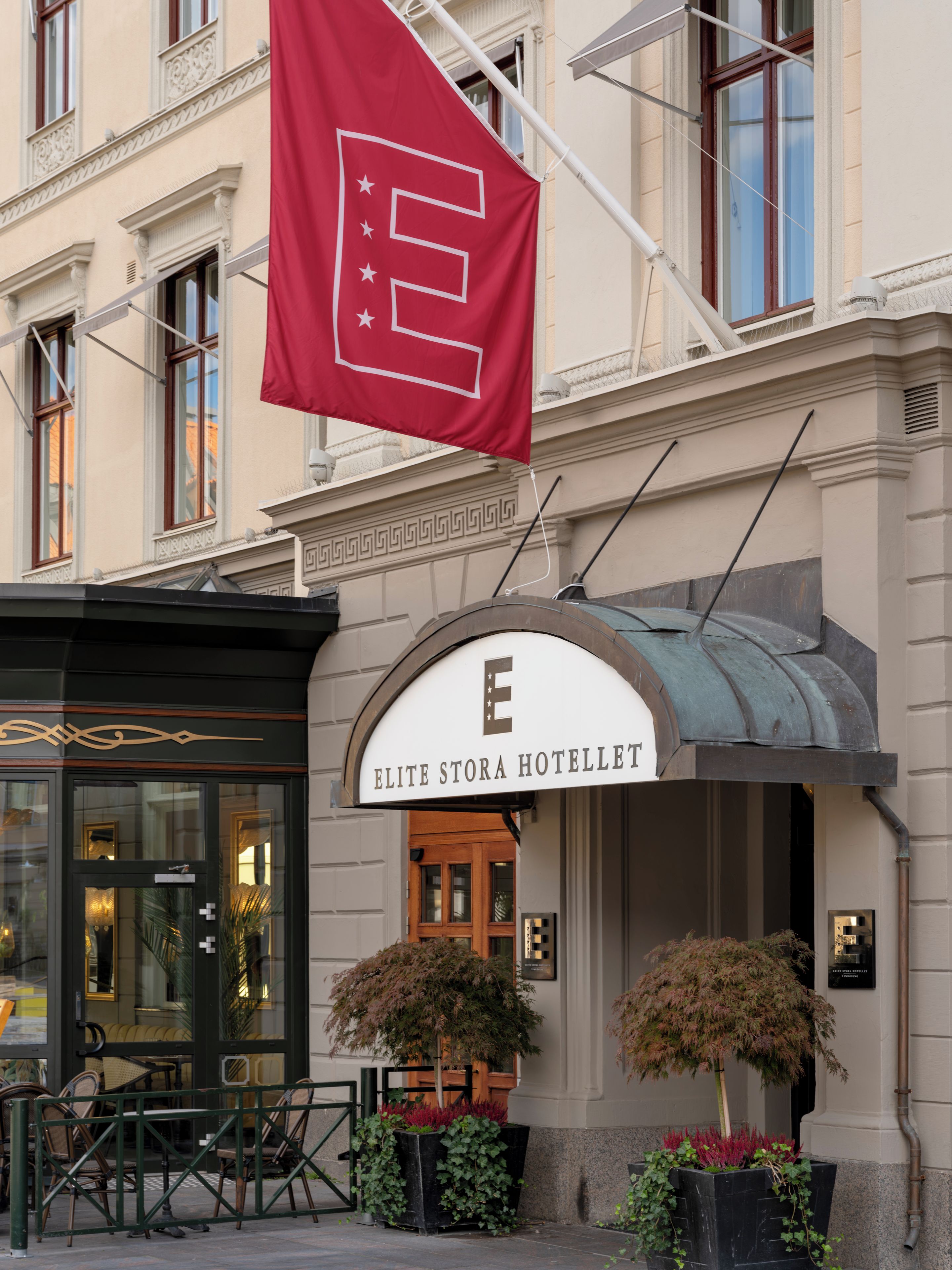El exterior del Hotel Elite Stora con un llamativo letrero con la letra 'E', estilo arquitectónico clásico y una bandera.