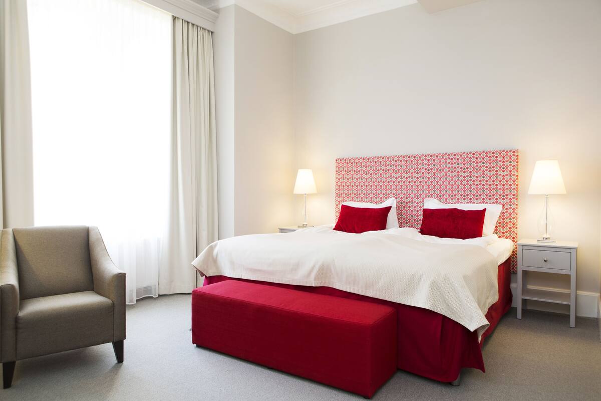 A hotel room with a bed, two bedside tables, a chair, and a window with curtains.