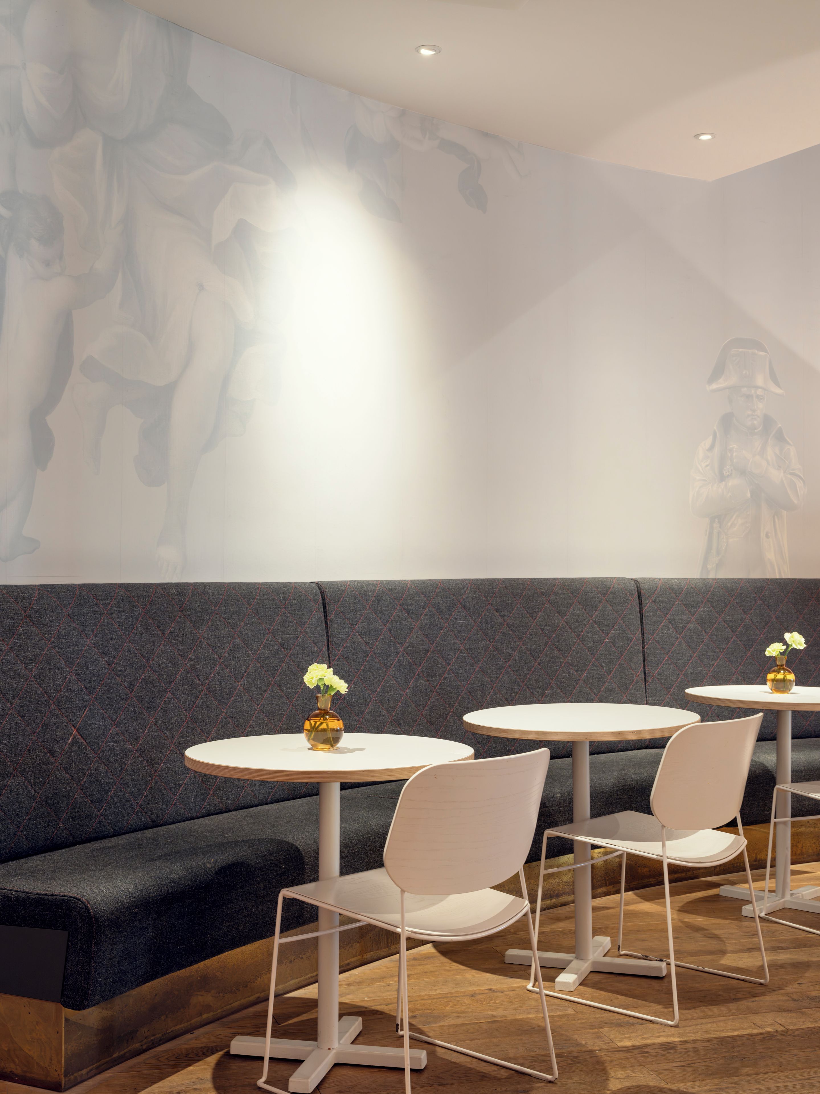 Un intérieur moderne avec un canapé à motifs foncés, des chaises blanches et des tables rondes, chacune agrémentée d’un vase de fleurs.