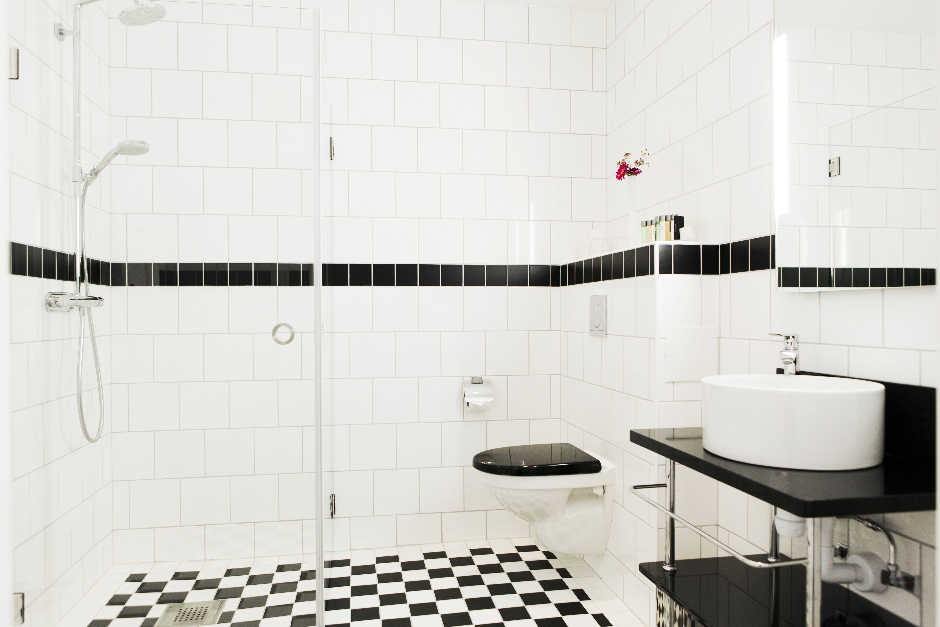 Un baño moderno con piso a cuadros blanco y negro, un lavamanos blanco y una ducha con cerramiento de vidrio.