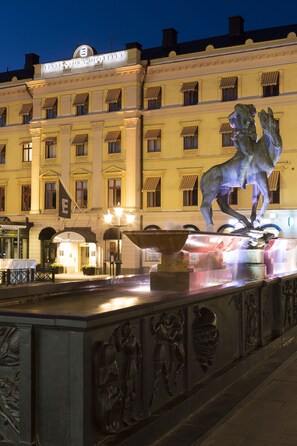 A fountain with a lion statue in front of a hotel with multiple windows and a sign. - Elite Stora Hotellet Linköping (Linkoping)