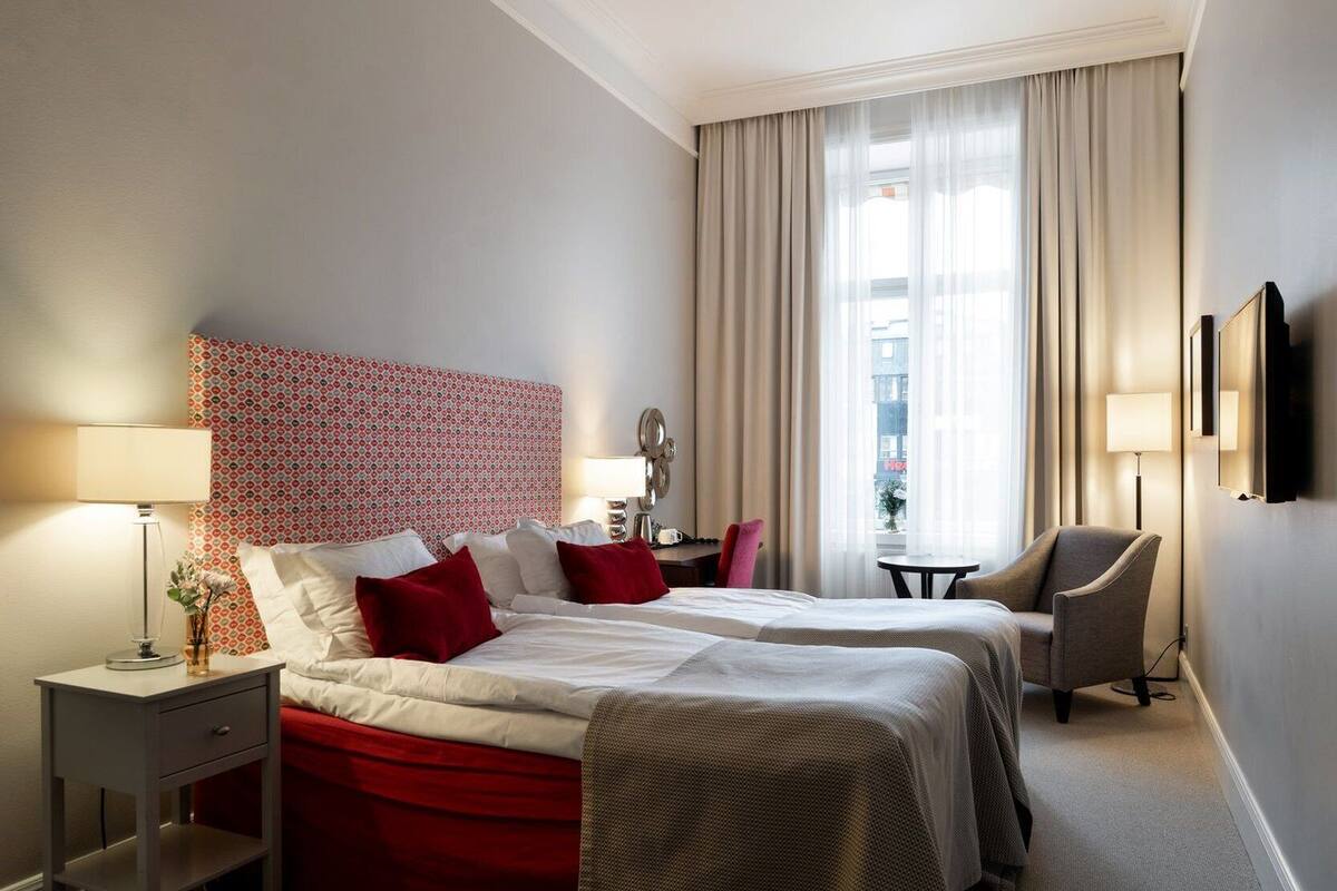A hotel room with two beds, a desk, a chair, a TV, and a window with curtains.