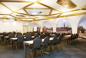 A conference room with tables and chairs, a high ceiling with geometric patterns, and murals of a cityscape on the walls.