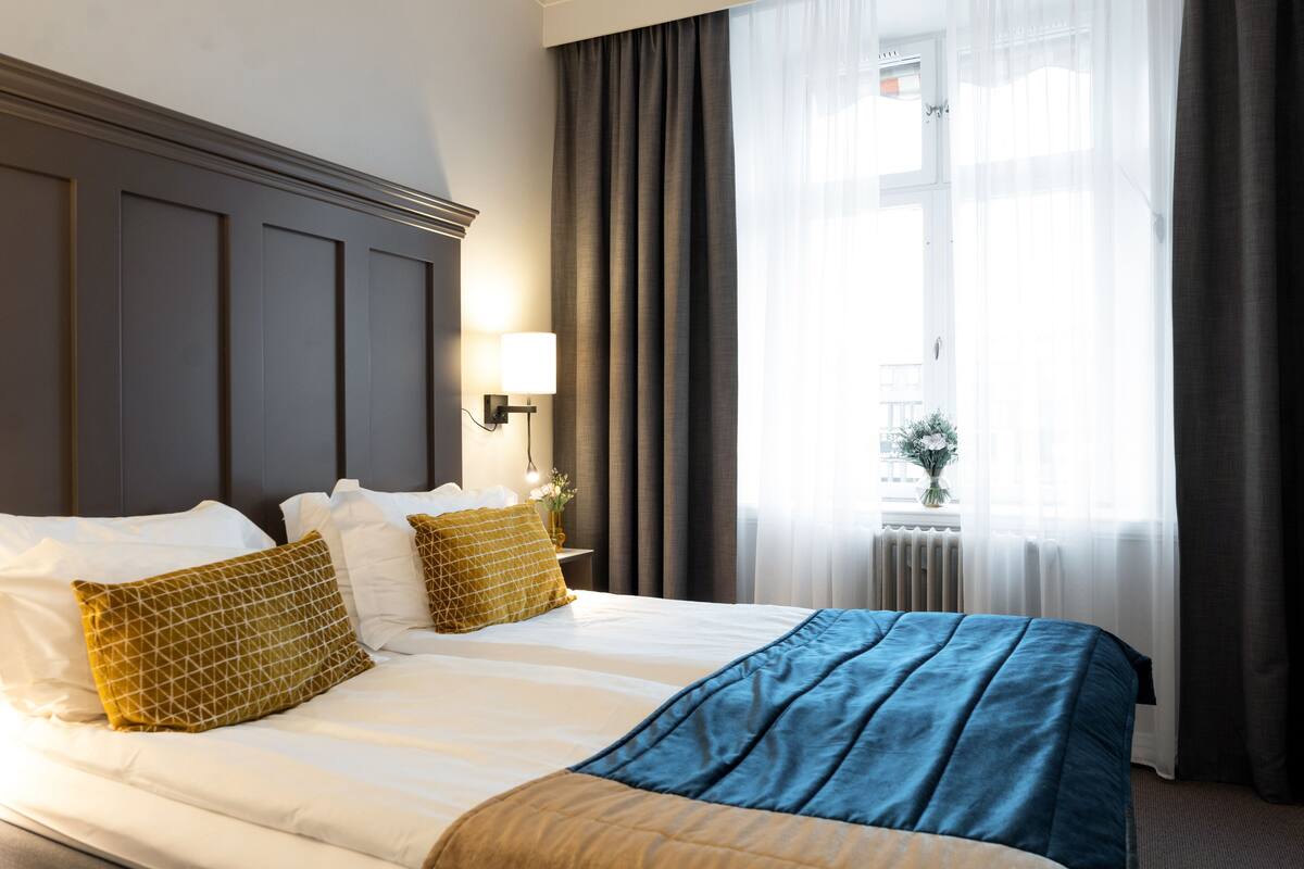 A hotel room with a large bed, a nightstand with a lamp, and a window with curtains.