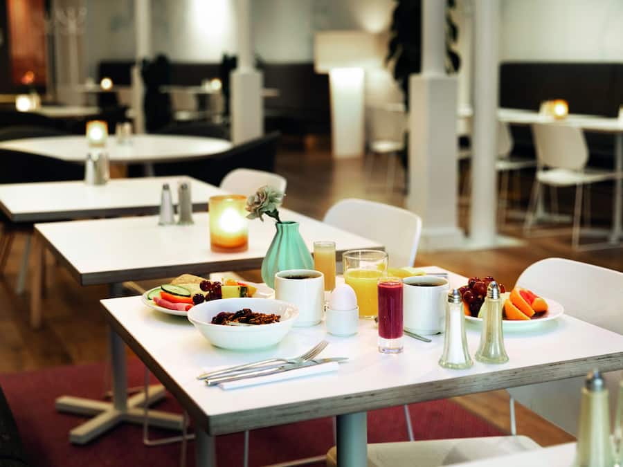 A dining area with tables set for breakfast, including bowls of cereal, fruits, and beverages.
