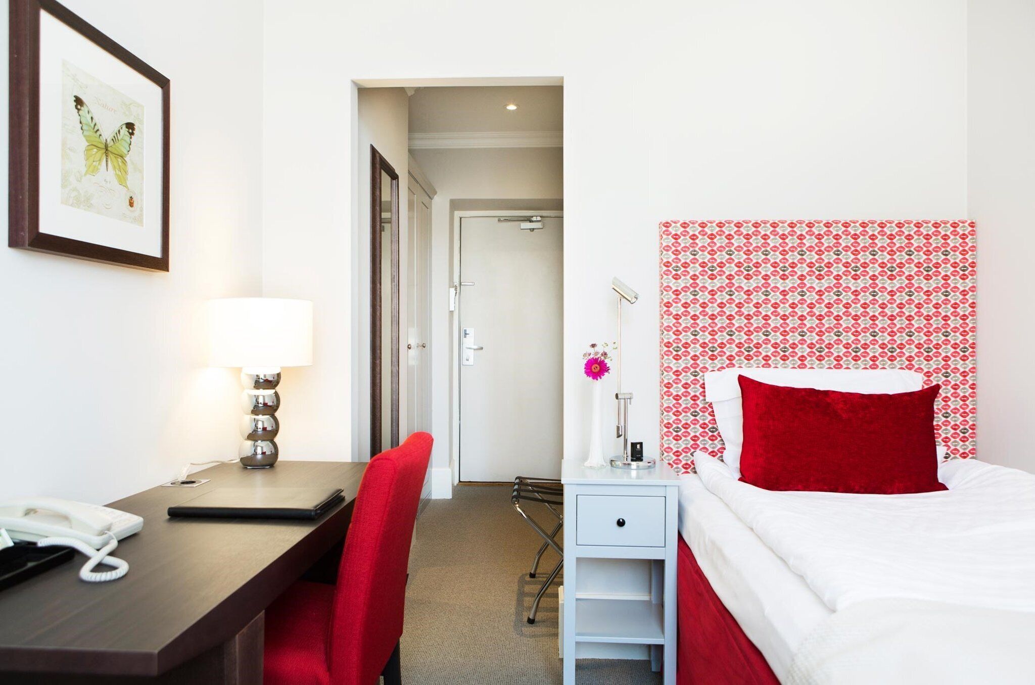 Habitación de hotel con escritorio, silla, cama y una obra de arte con una mariposa enmarcada.