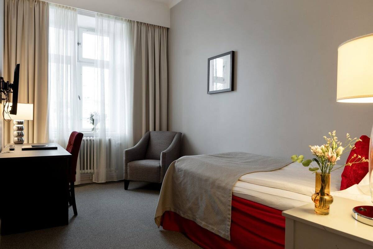 A hotel room with a bed, a desk, a chair, a lamp, and a picture on the wall.