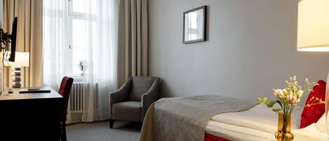 A hotel room with a bed, a desk, a chair, a lamp, and a picture on the wall.