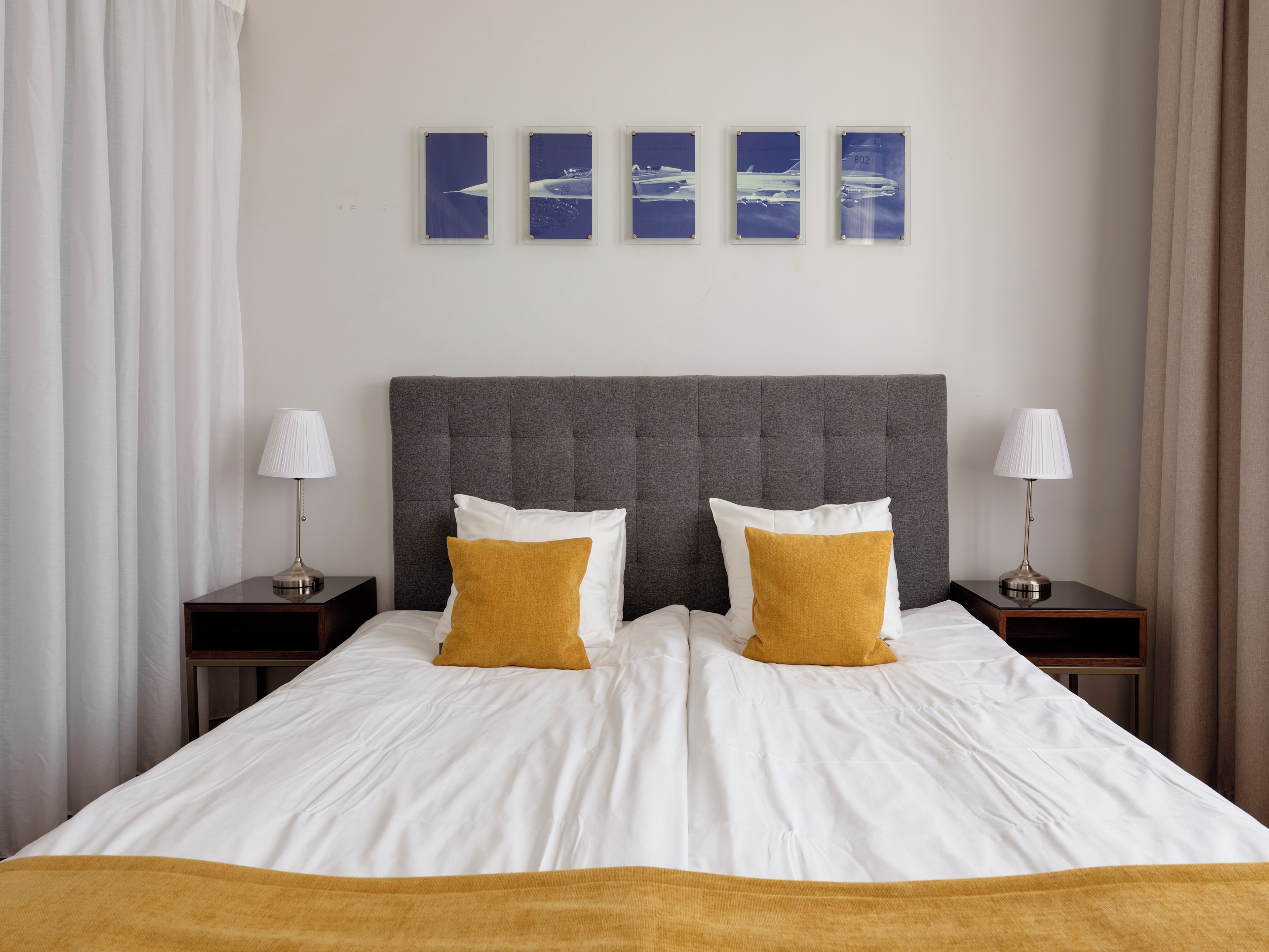 Una habitación de hotel con una cama grande, dos lámparas de noche, un cabecero y cuatro cuadros en la pared.