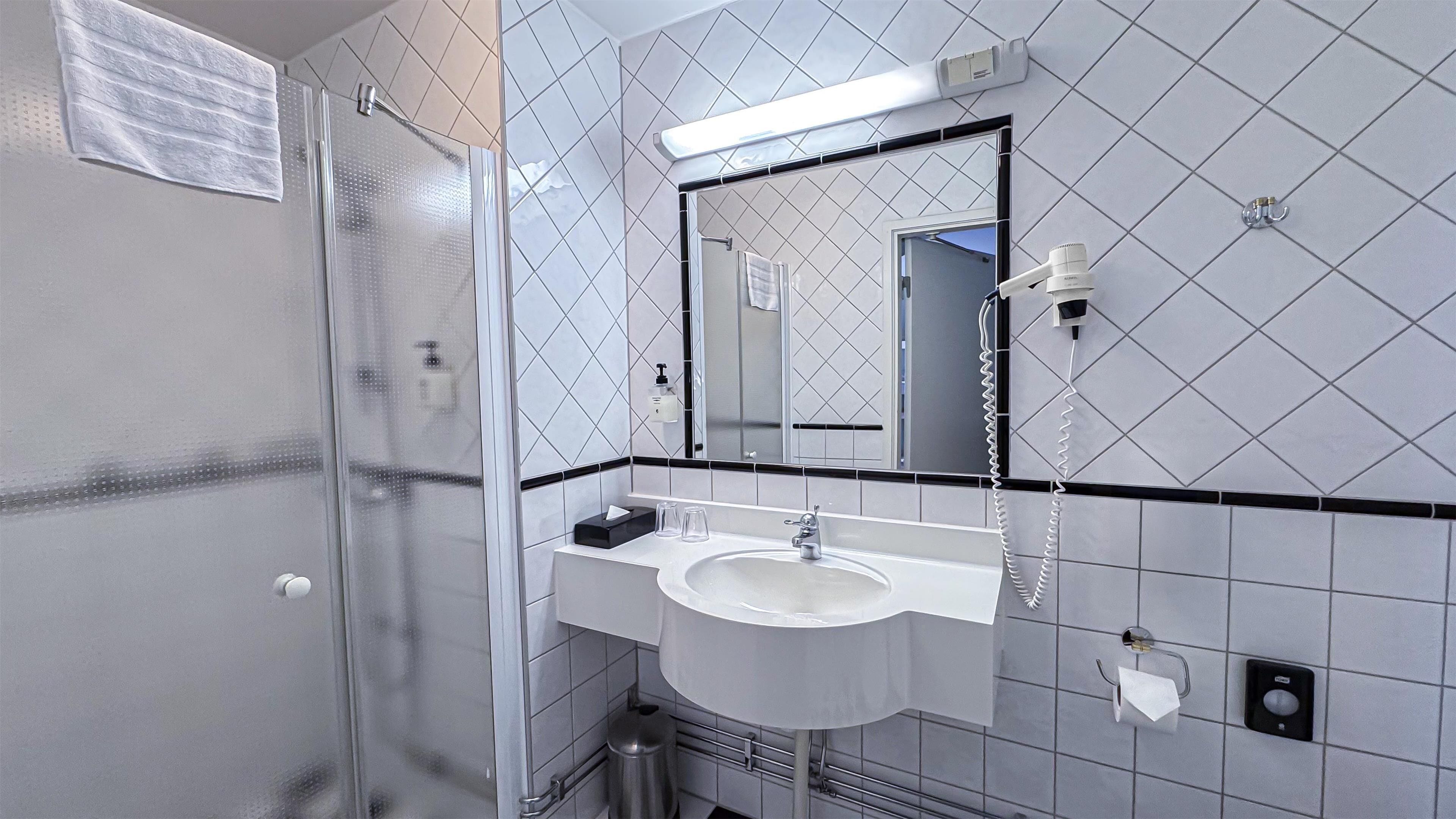 A bathroom with a glass shower enclosure, a white sink, a mirror, and a towel rack.