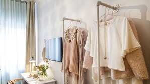 Une chambre bien rangée, avec un portant à vêtements, une table de chevet avec une lampe et un téléviseur fixé au mur.
