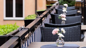 Espace extérieur aménagé avec des chaises en osier, une table ornée d’un vase de fleurs et une plante en pot.