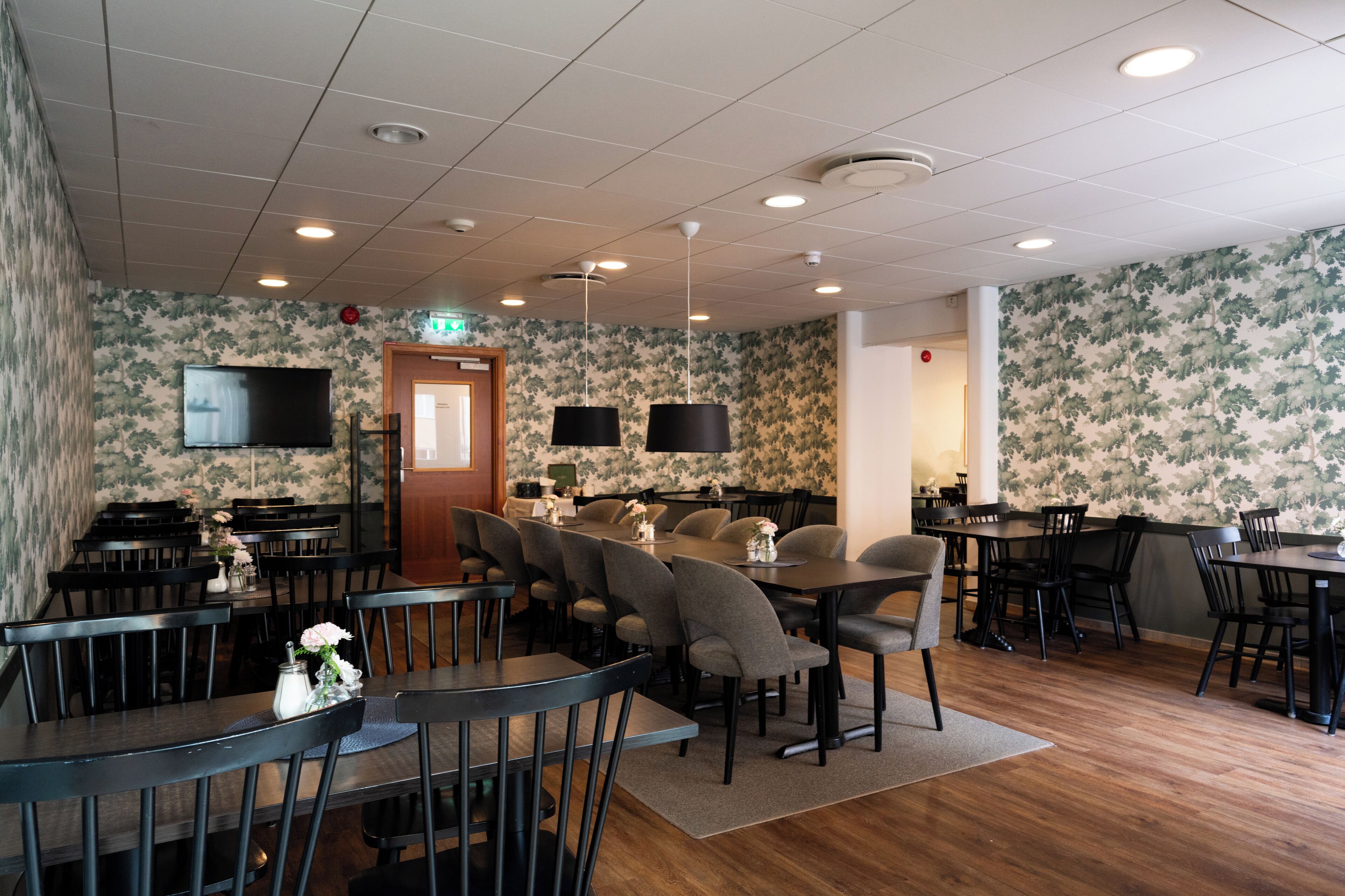Un restaurant avec plusieurs tables et chaises, un téléviseur fixé au mur et un papier peint à motifs.