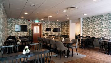A restaurant with multiple tables and chairs, a television mounted on the wall, and a patterned wallpaper.