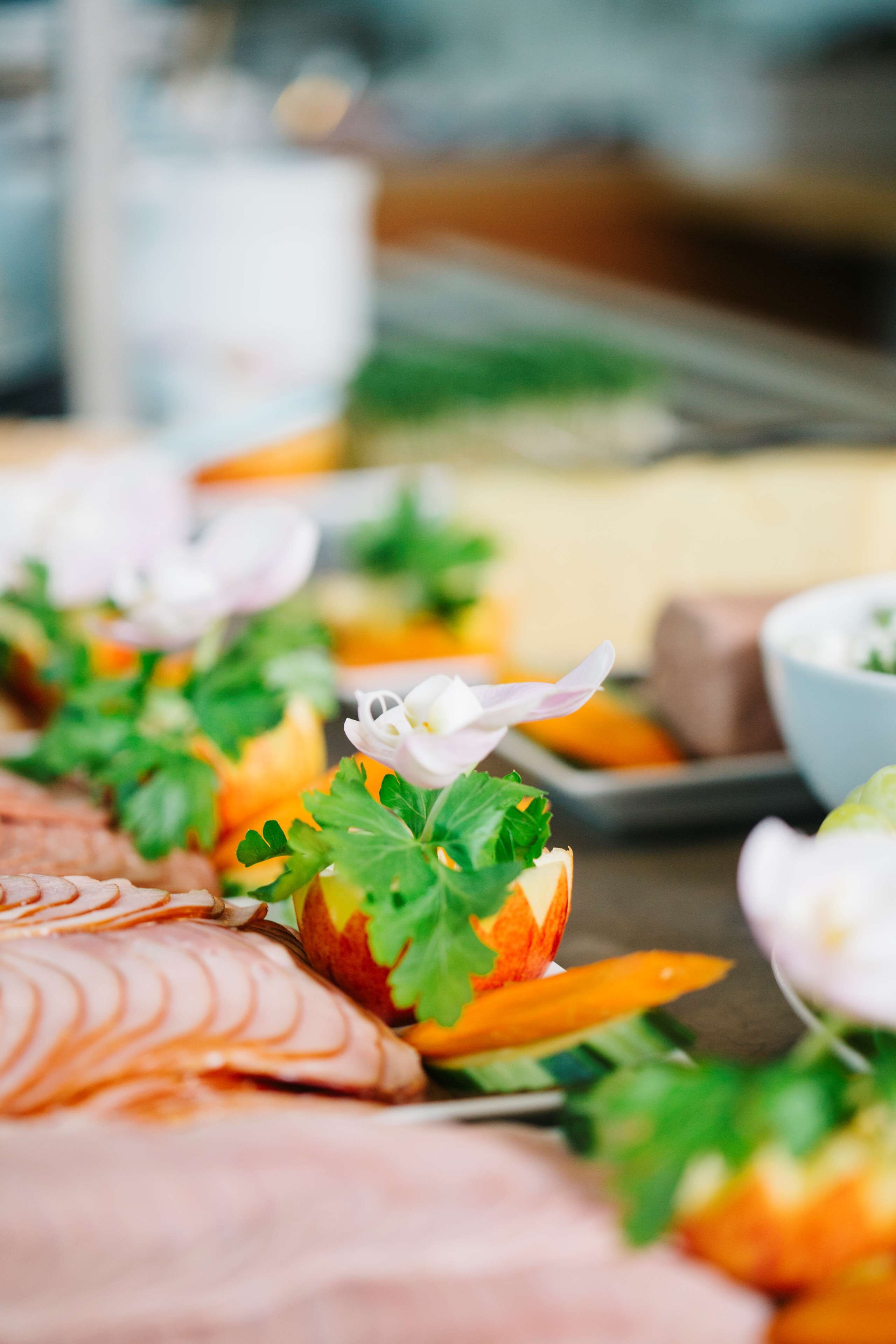 Una mesa de buffet con carnes en rodajas, adornada con hierbas frescas y flores.