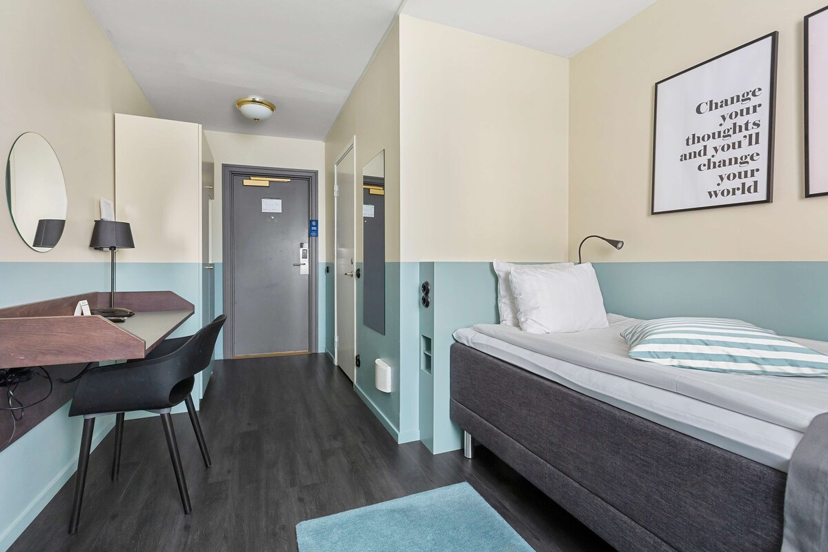 Ein modernes Hotelzimmer mit Schreibtisch, Stuhl, Bett und einem motivierenden Zitat an der Wand.