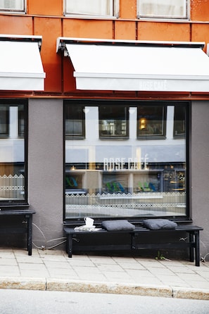 A café with a black bench outside, a window with a metal railing, and a sign that reads "ROSE CAFE".