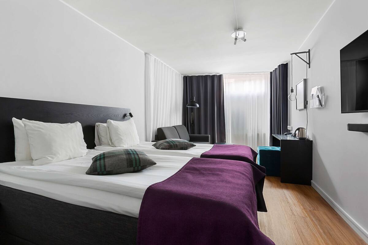 Una camera d'albergo con un letto grande, due comodini, una scrivania e una televisione.