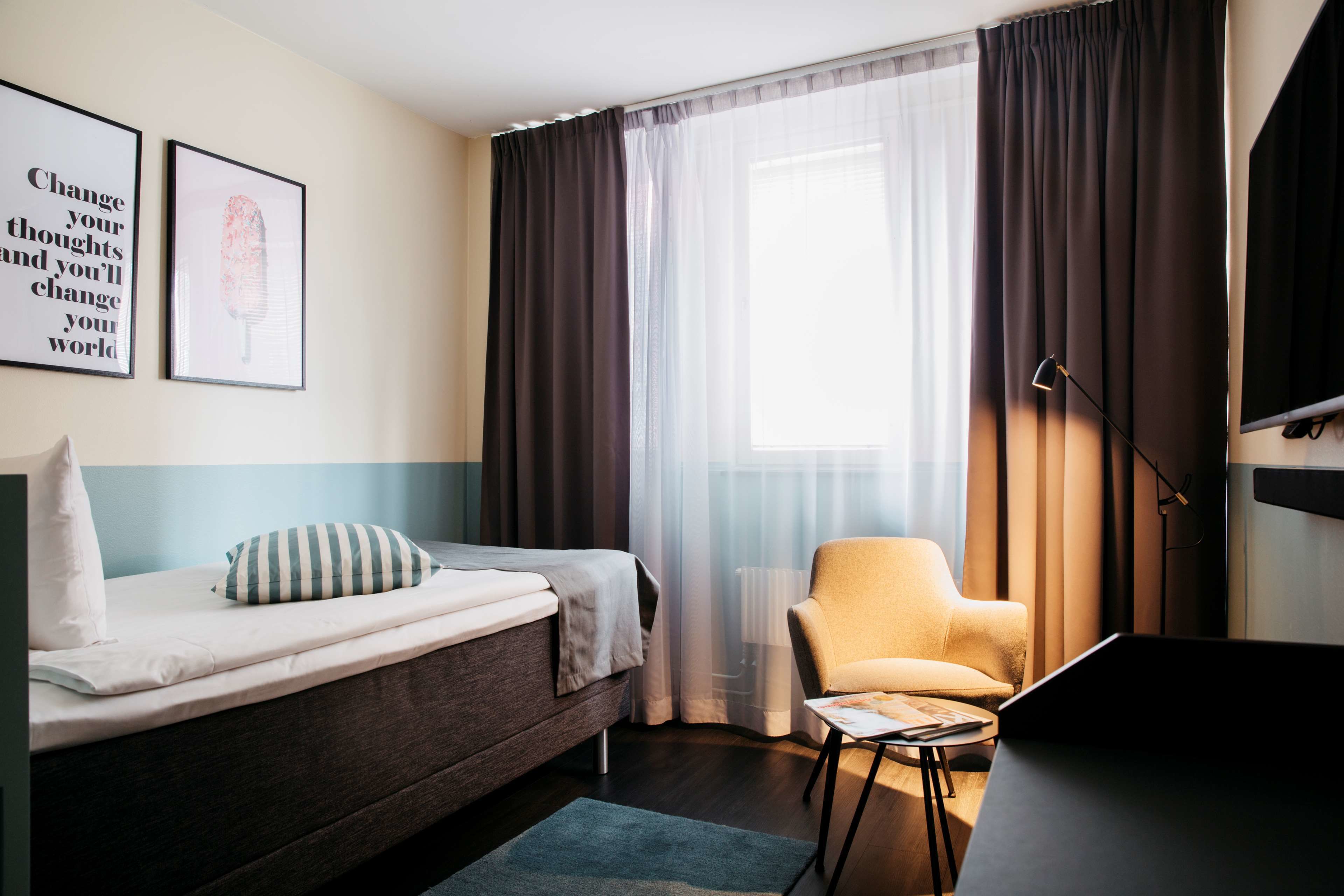 Una habitación de hotel moderna con cama, una silla, escritorio y un ventanal con cortinas.