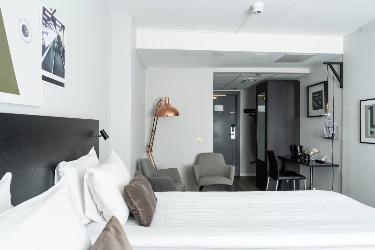 Una camera d'albergo moderna con un ampio letto, una scrivania, due poltrone e una lampada.