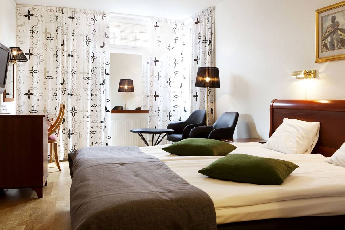 Una camera d'albergo con un letto, due poltrone, una scrivania e due lampade.
