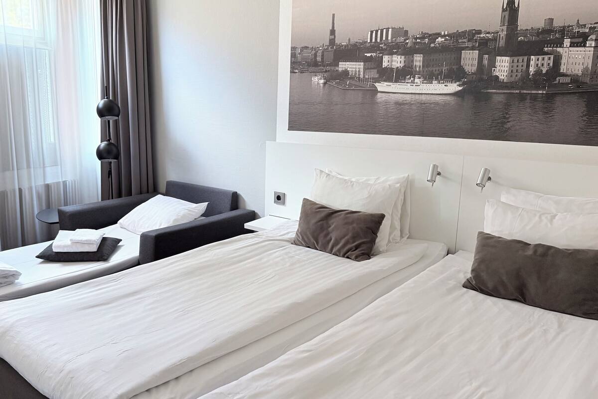 Camera d'albergo con due letti, un divano e vista sulla città.