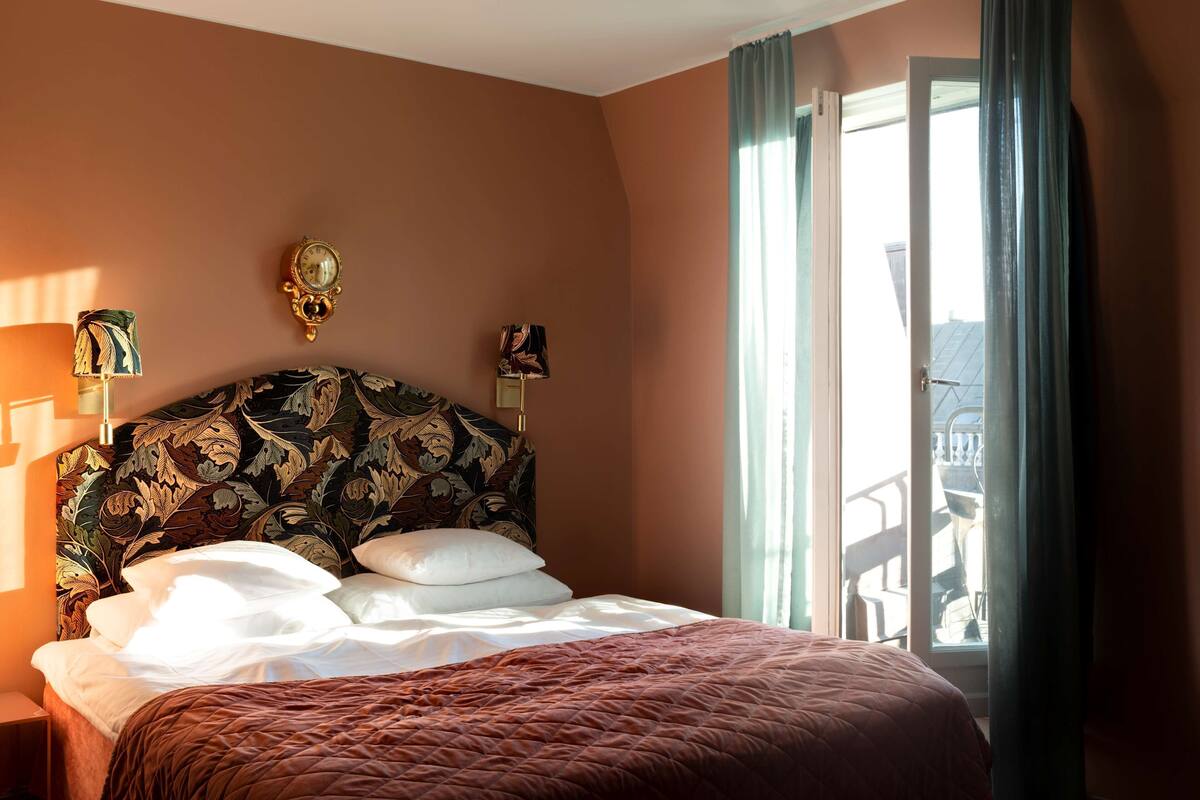 A hotel room with a large bed, a wall clock, and a view of the outside balcony.