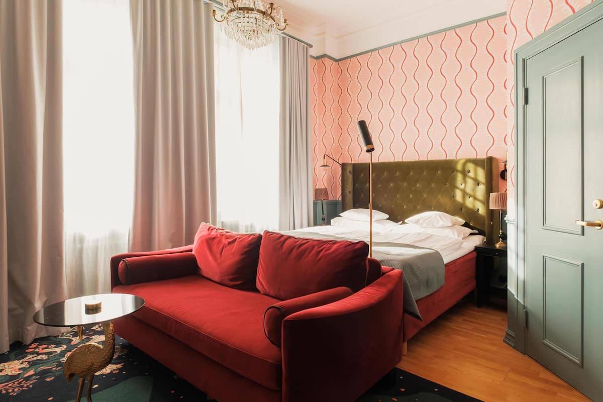 A room with a red sofa, a bed with a headboard, a small table, and a door.