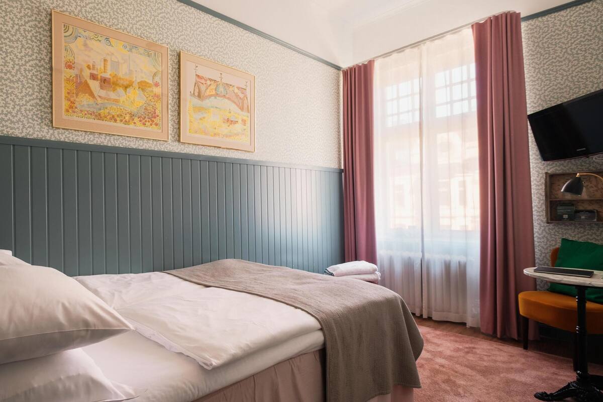A bedroom with a bed, a chair, a television, and two framed pictures on the wall.