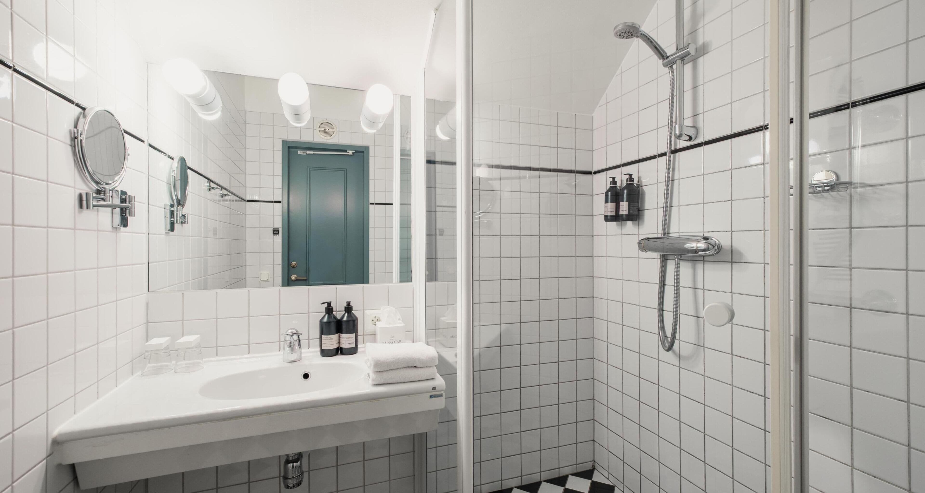 A bathroom with a sink, mirror, two bottles of shampoo, and a shower.