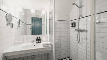 A bathroom with a sink, mirror, two bottles of shampoo, and a shower.
