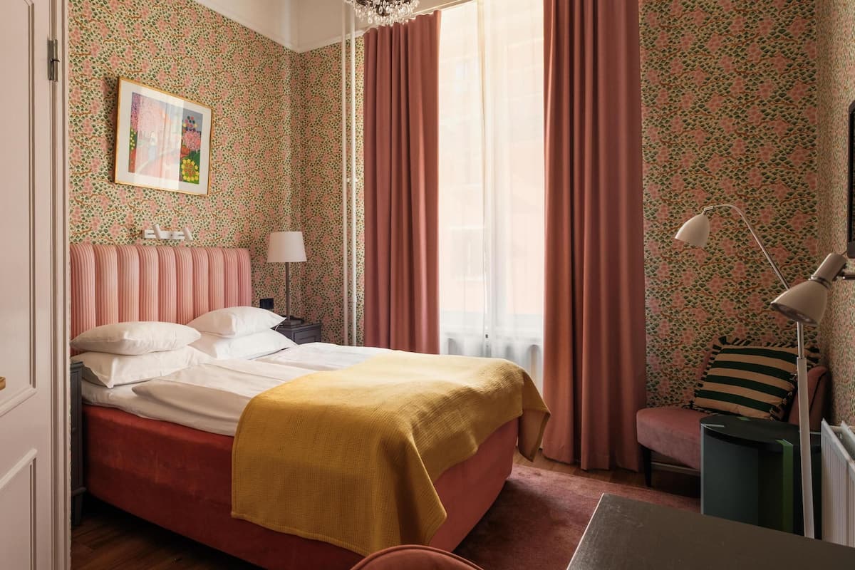 A bedroom with a bed, a bedside table, a lamp, a chair, and a window with curtains.