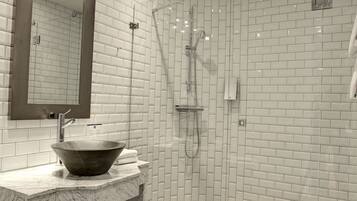 Un baño moderno con lavamanos de mármol, un espejo grande y zona de ducha.