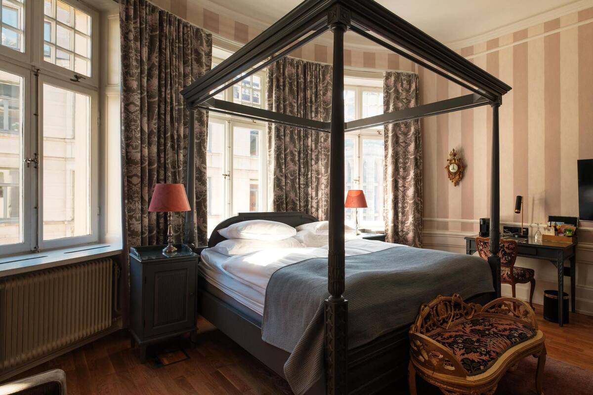 A four-poster bed with a canopy, a television, a desk with a chair, and a radiator.