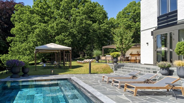 A swimming pool with lounge chairs and a covered seating area. - Villa Lovik (Lidingo)