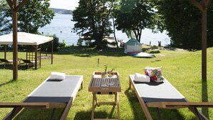A covered outdoor seating area with two lounge chairs, a table with a tray of items, and a view of a lake and trees. - Villa Lovik (Lidingo)