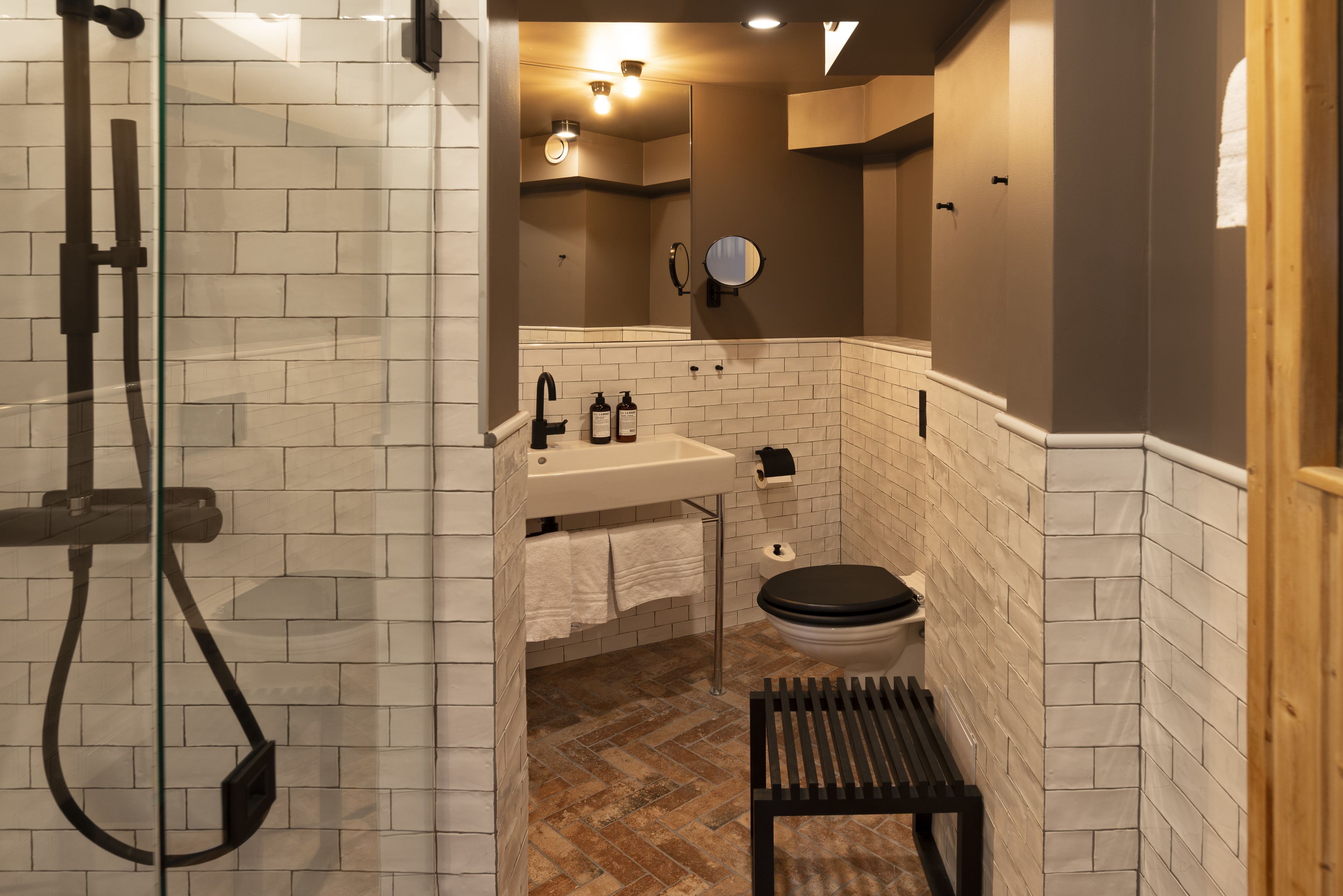 Un baño moderno con ducha vidriada, lavamanos con artículos de aseo y retrete.