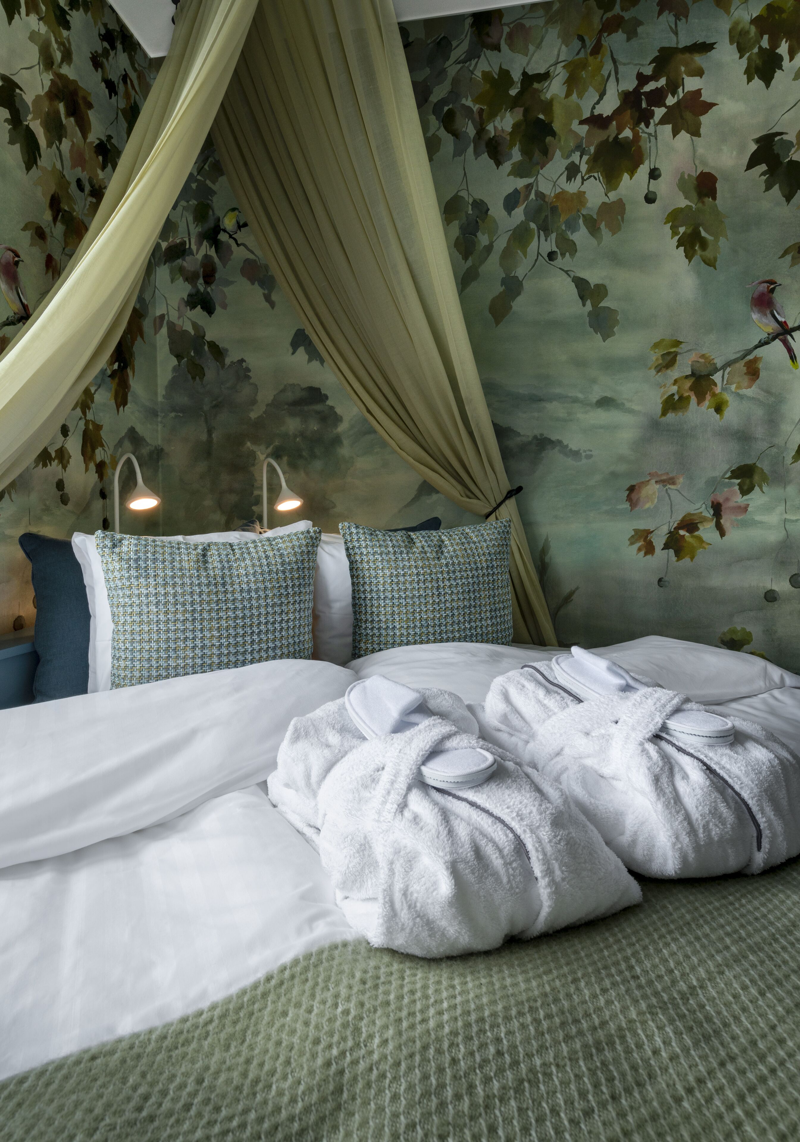 A bed with white linens, green patterned pillows, and a green textured blanket.