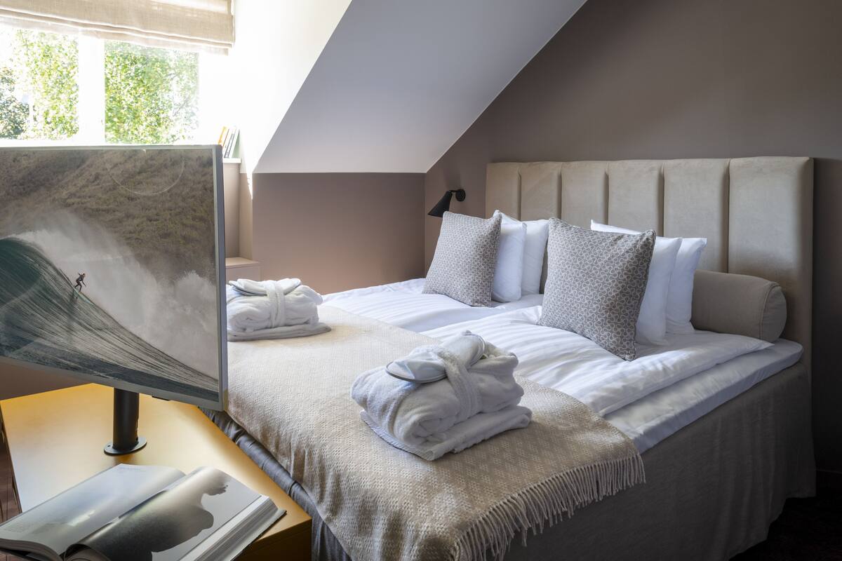 A hotel room with a bed, a desk with a computer, and a window with a view of trees.