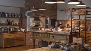 Una cocina rústica con pared de ladrillo, armarios de madera y una variedad de panes y pasteles expuestos en estantes y encimeras.