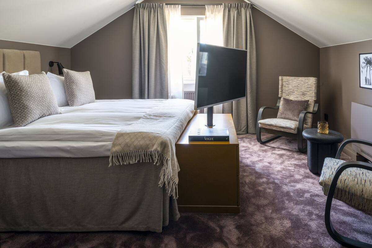 A hotel room with a large bed, a flat-screen TV, a chair, and a small table.