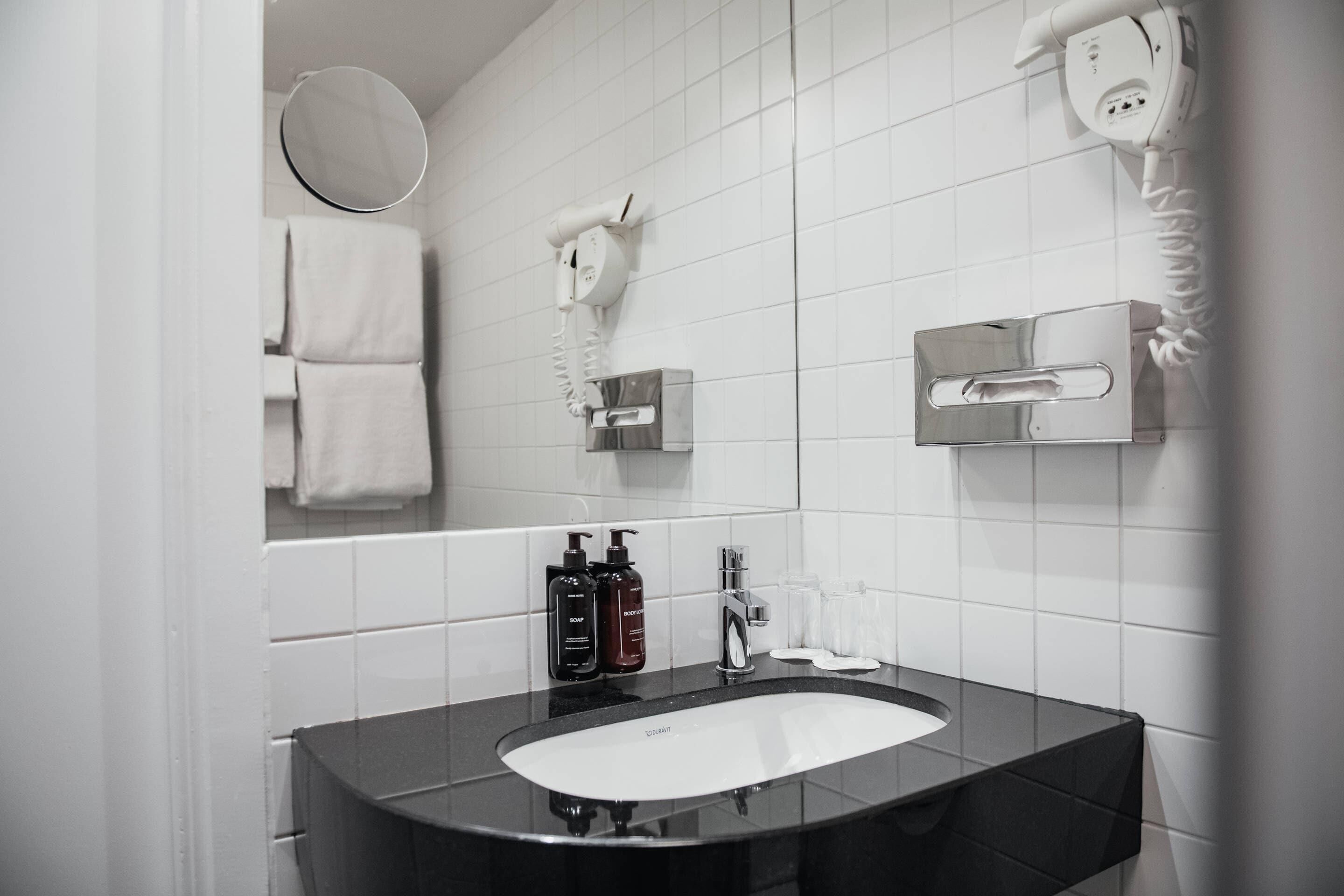 A modern bathroom with a black sink, white tiles, a hairdryer, and a mirror.