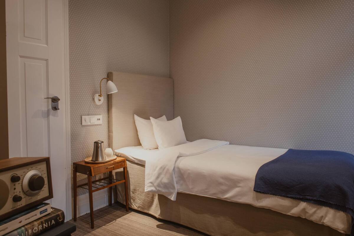 Un dormitorio con cama, mesita de noche, lámpara y radio.