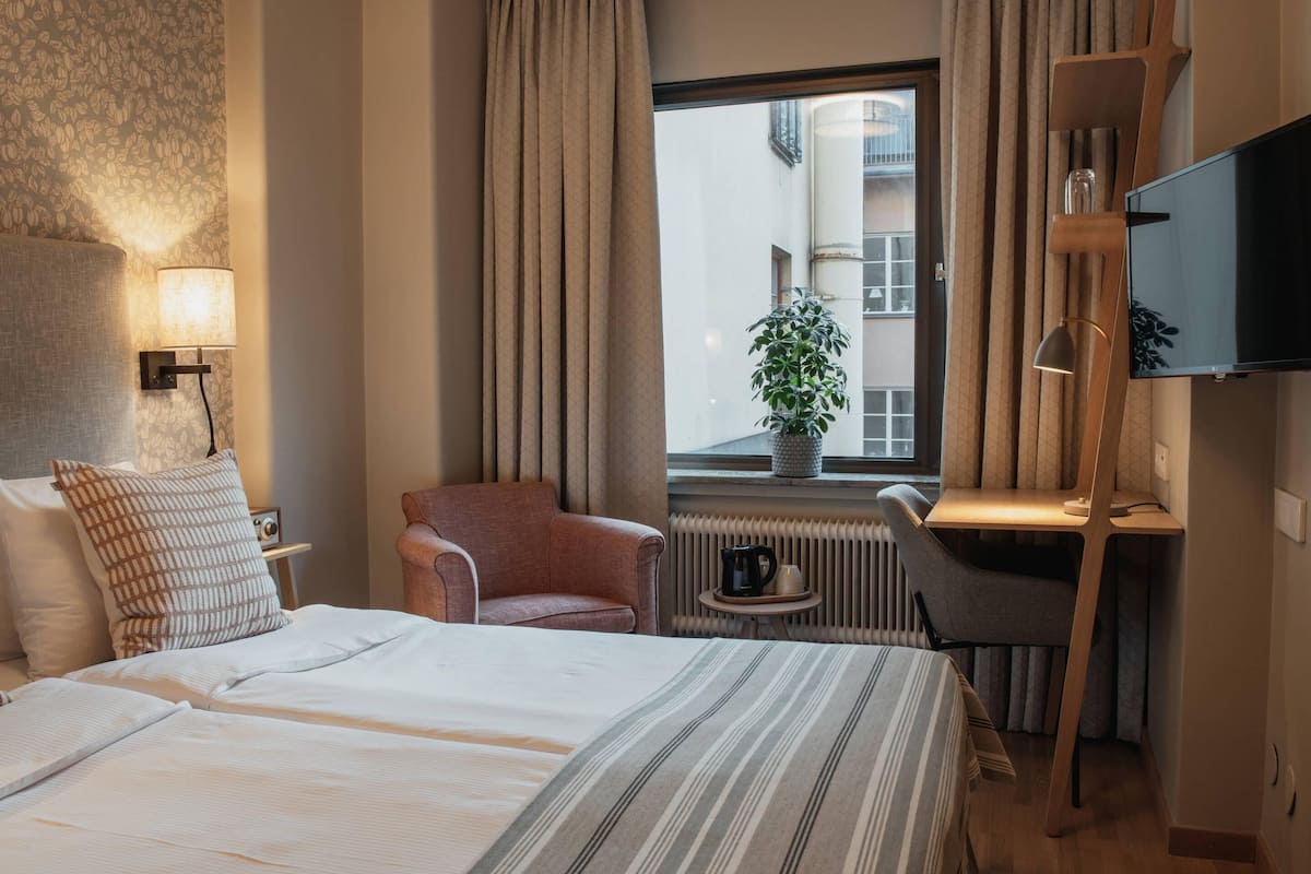 Habitación de hotel con cama, escritorio, silla, televisión y ventana con vistas a edificios.