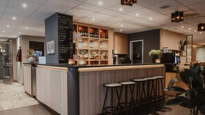 Una zona de bar con mostrador de madera, taburetes y estanterías llenas de botellas y vasos.