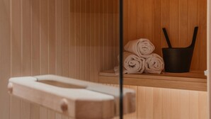 Una sauna de madera con un banco, un estante con toallas enrolladas y un cubo negro.